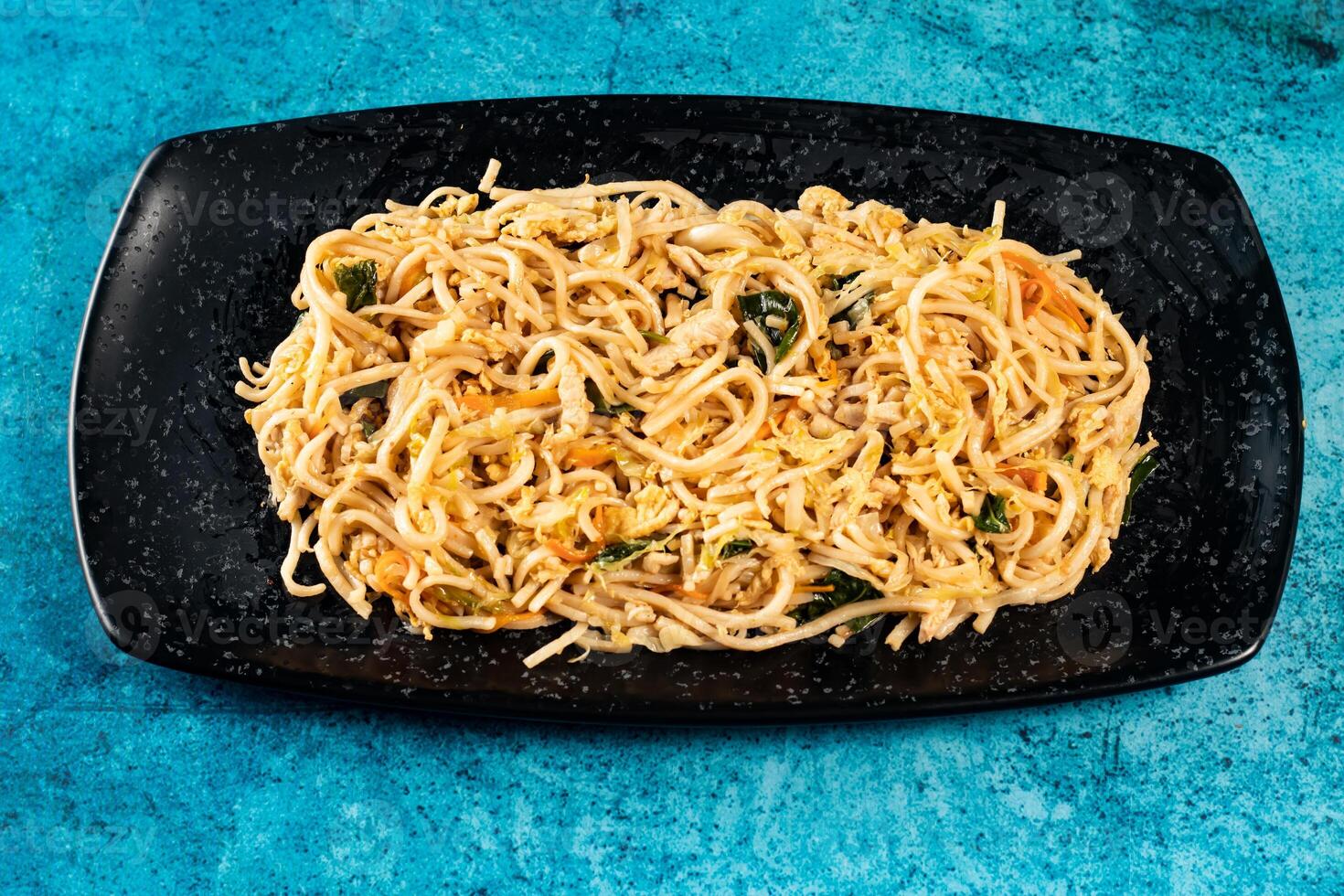 Spicy vegetable chow mein in a black tray isolated on marble background top view of chinese food photo