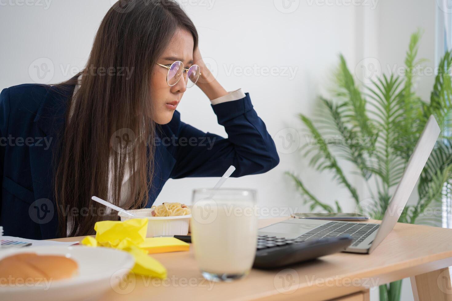 mujer de negocios ocupada y cansada comiendo espagueti para el almuerzo en la oficina y trabajando para entregar estados financieros a un jefe. con exceso de trabajo y poco saludable para comidas preparadas, concepto de agotamiento. foto