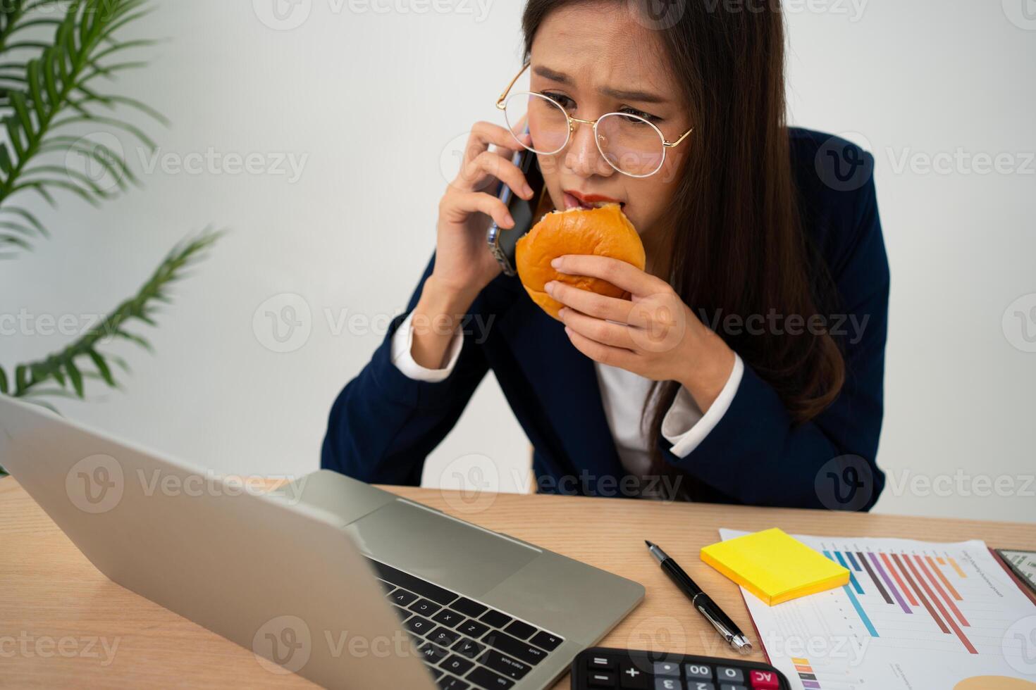 ocupado y cansado mujer de negocios comiendo un pan y Leche para almuerzo a el escritorio oficina y trabajando a entregar financiero declaraciones a un jefe. sobrecargado de trabajo y insalubre para Listo comidas, agotamiento concepto. foto