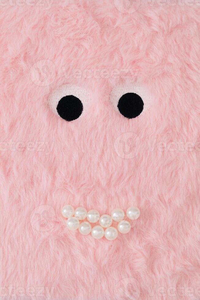 Cute fluffy monster made with pastel pink faux fur and white pearls. Minimal concept. Creative funny face composition. An original cute fluffy monster background image idea. Flat lay, top of view. photo