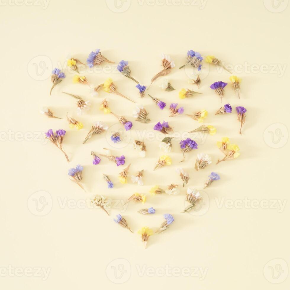 Heart shape made of colorful dry flowers on pastel cream background. Romantic floral greeting card. Minimal love concept and simplicity. Nature decorative design. Flat lay. photo