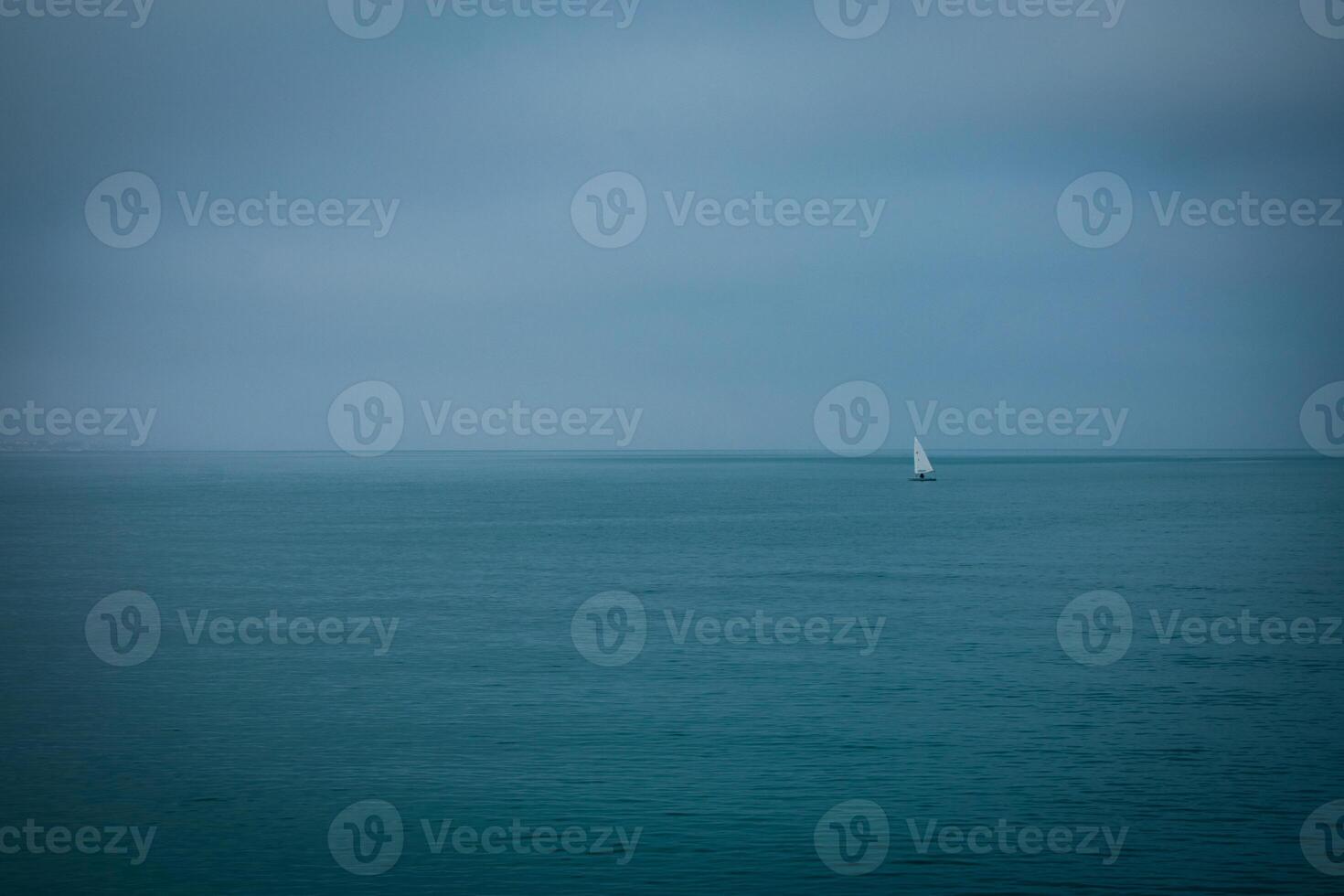 playa paisaje con nublado clima y un pequeño barco en el horizonte - mínimo panorama ver de el tormenta oscuro melancólico imagen foto