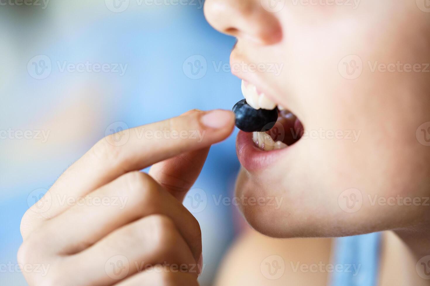 Unrecognizable girl biting fresh organic blueberry at home photo