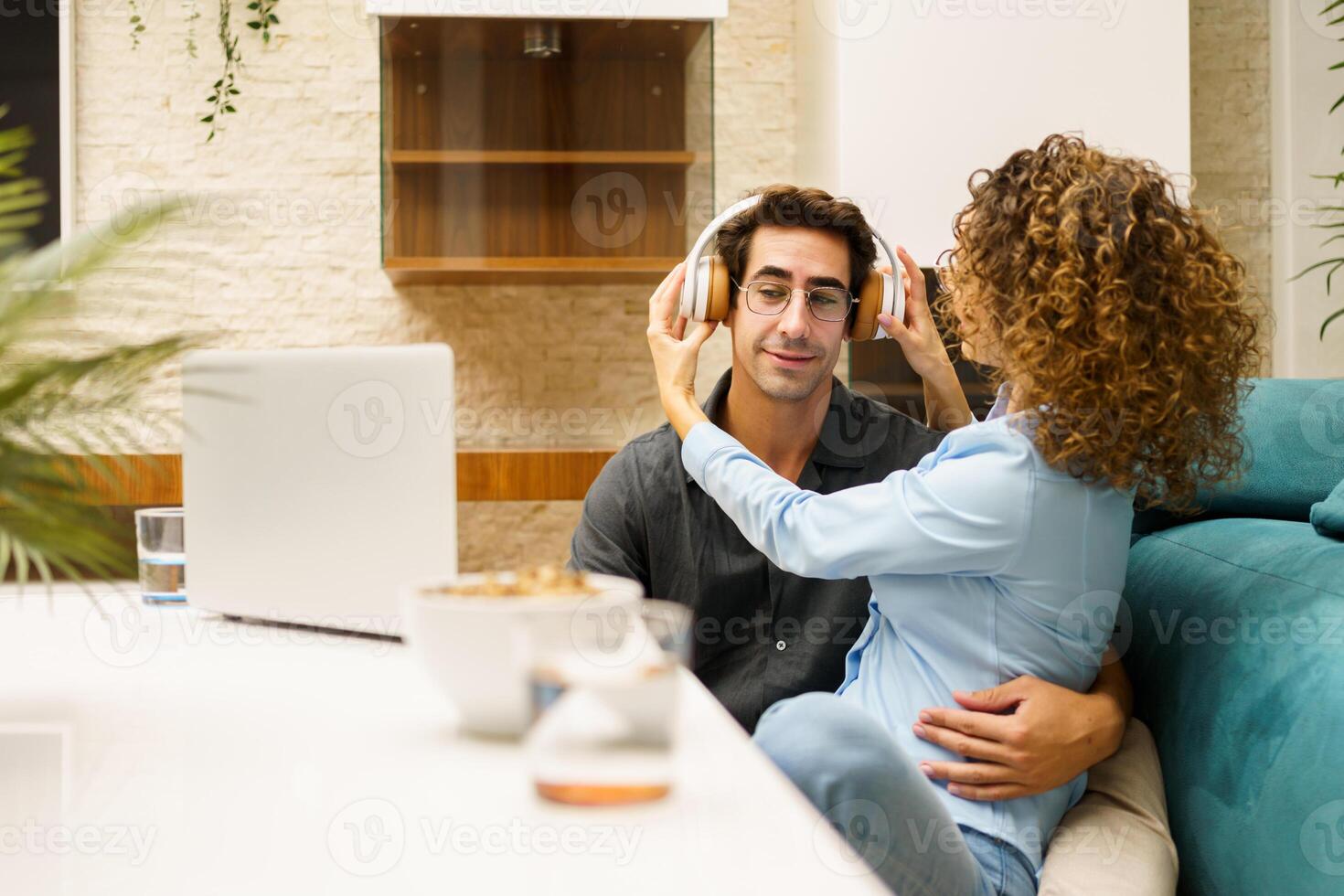 Loving couple playing with headphones while spending time together in living room photo