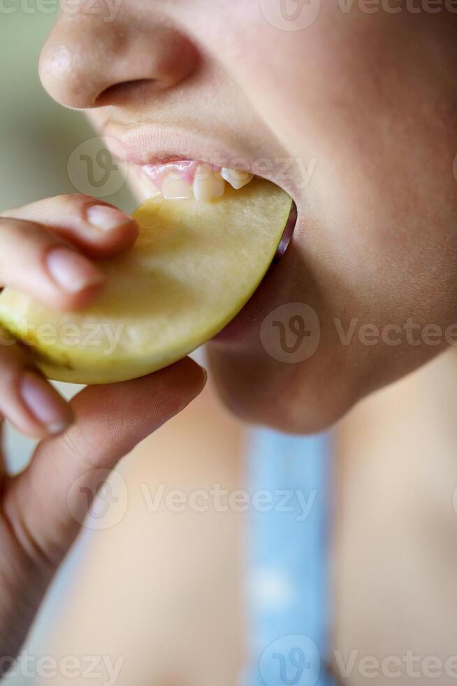 Crop teenage girl biting fresh juicy apple slice at home photo