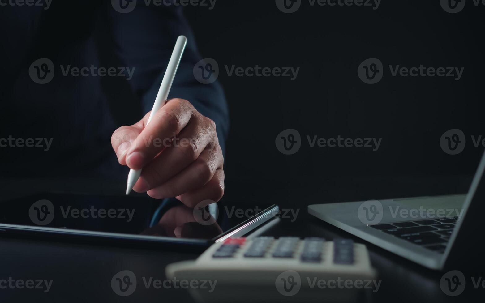 Businessman in black suit working on laptop computer and tablet and calculator, Hand Hands touch on tablet at office with dark background, Online working, Close up, Copy space. photo