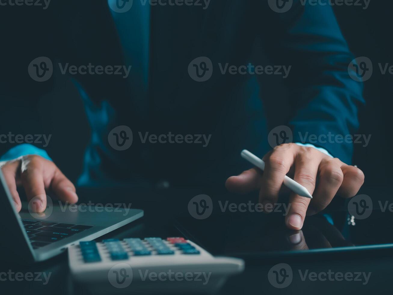 Businessman in black suit working on laptop computer and tablet and calculator, Hand Hands touch on tablet at office with dark background, Online working, Close up, Copy space. photo