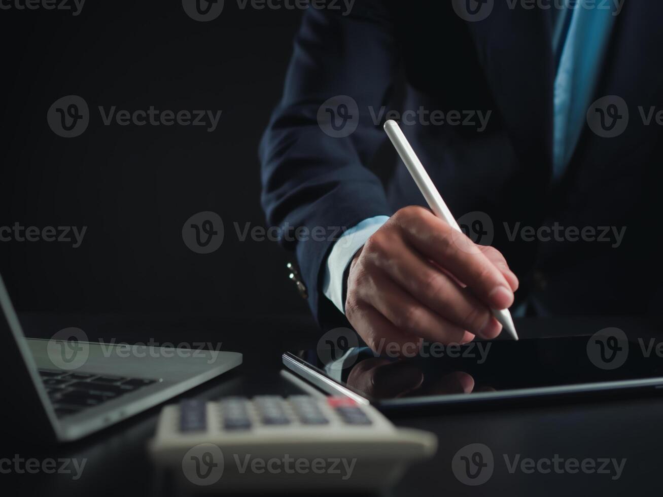 Businessman in black suit working on laptop computer and tablet and calculator, Hand Hands touch on tablet at office with dark background, Online working, Close up, Copy space. photo