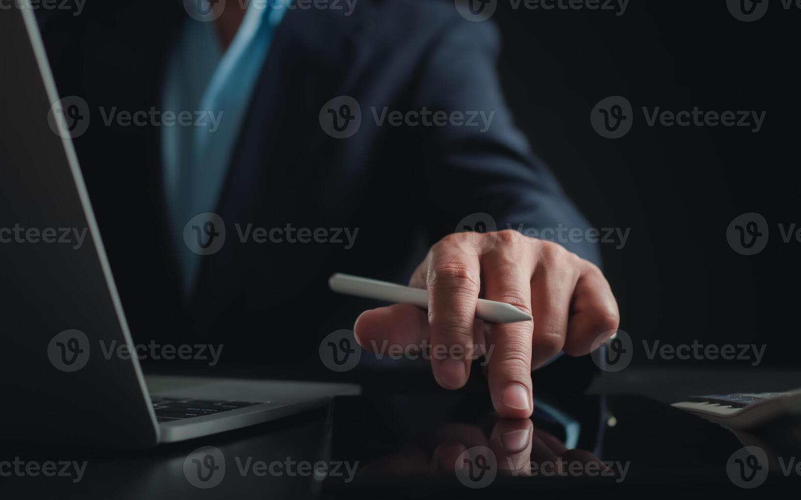Businessman in black suit working on laptop computer and tablet, Hand Hands touch on tablet at office with dark background, Online working, Close up, Copy space. photo