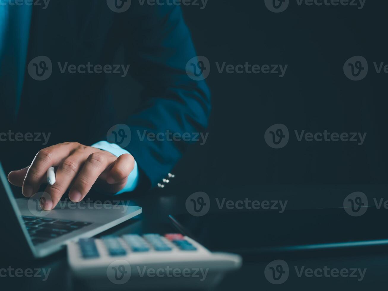 Businessman in black suit working on laptop computer and tablet and calculator, Hand Hands touch on tablet at office with dark background, Online working, Close up, Copy space. photo