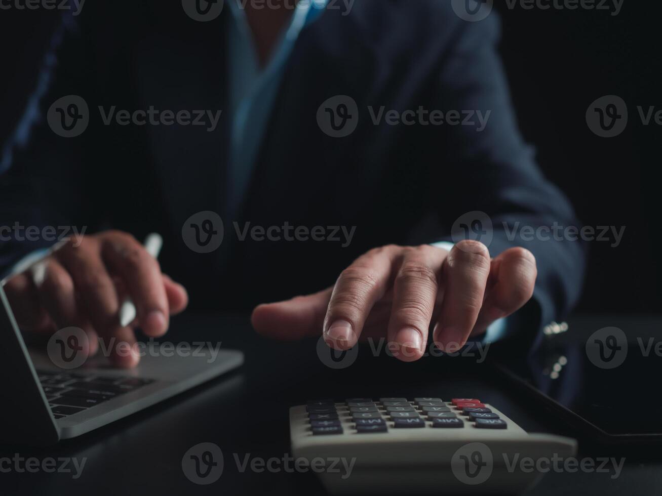 Businessman in black suit working on laptop computer and tablet and calculator, Hand Hands touch on tablet at office with dark background, Online working, Close up, Copy space. photo
