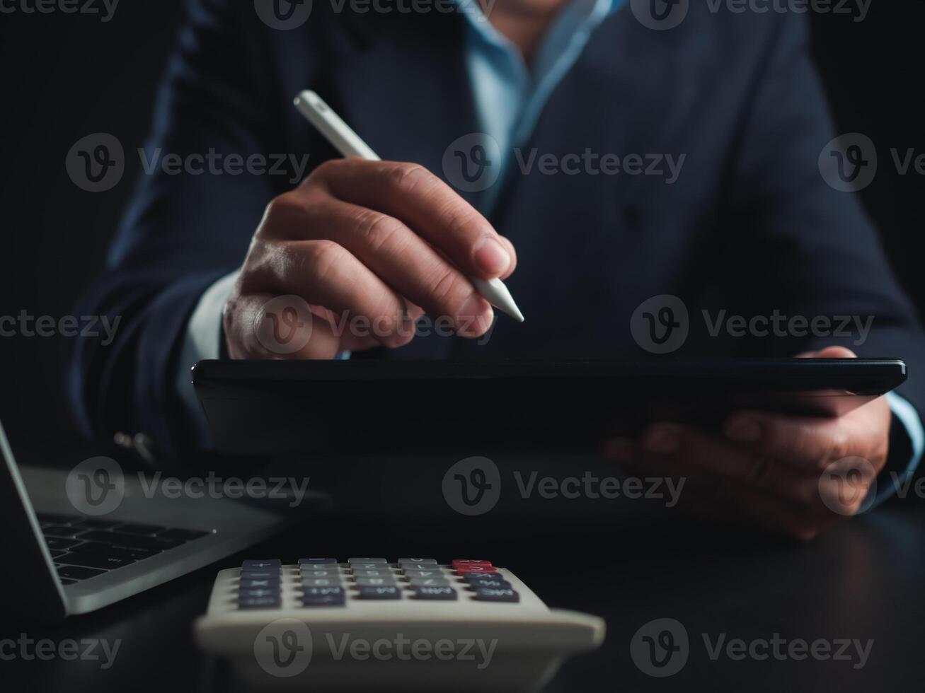 Businessman in black suit working on laptop computer and tablet and calculator, Hand Hands touch on tablet at office with dark background, Online working, Close up, Copy space. photo