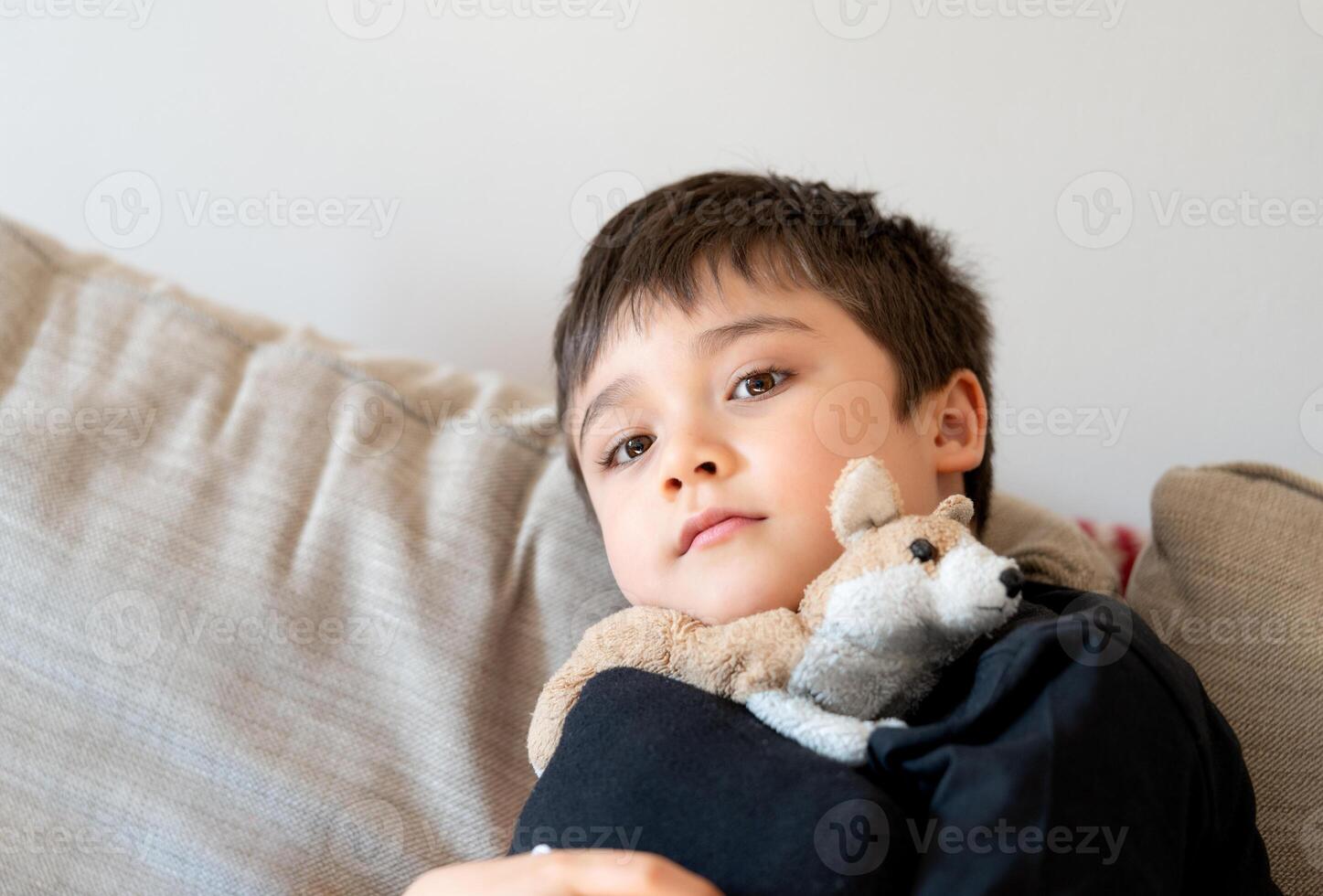 niño chico sentado en sofá, cerrar arriba sincero retrato linda colegio acecho televisión en fin de semana.positivo niño relajante a hogar después colegio foto