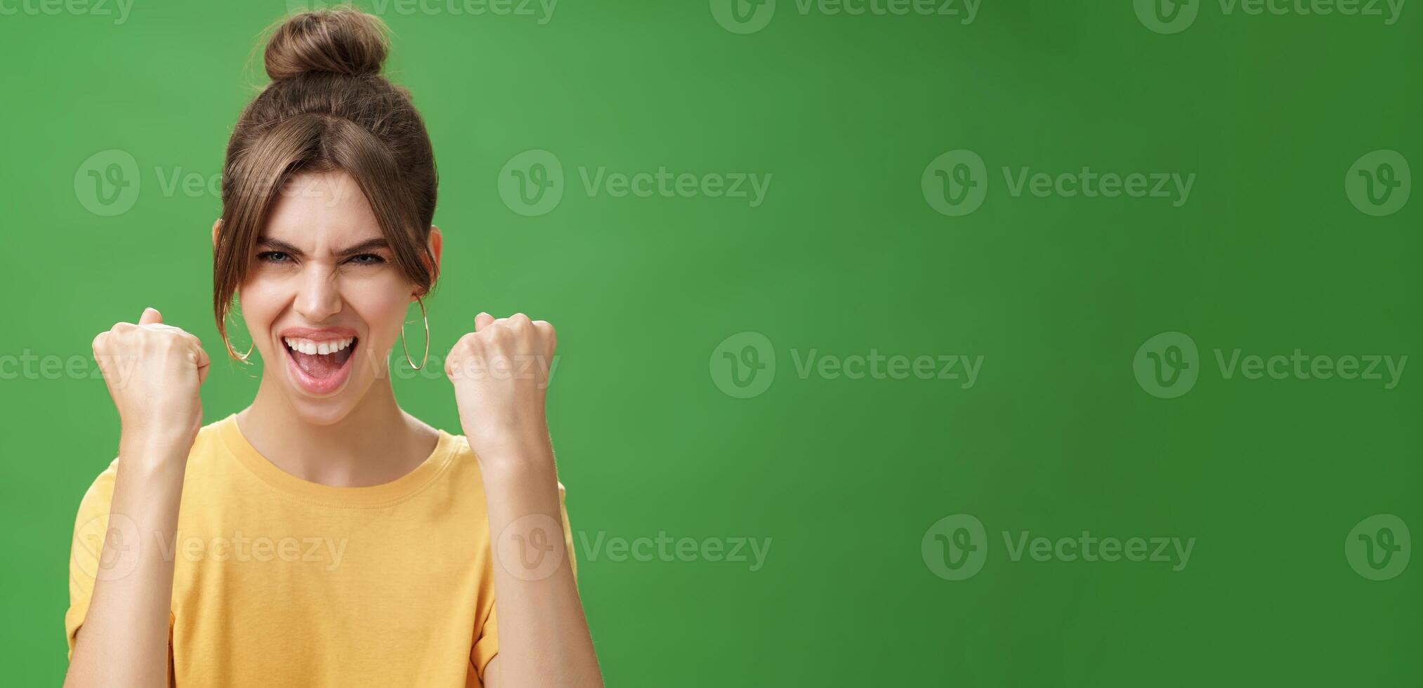 mujer con espíritu de ganador levantamiento apretado puños sonriente emocionado y apoyo aplausos siendo Listo para gimnasio ejercitado abucheos confidentes con grito mirando atrevido a cámara terminado verde pared foto