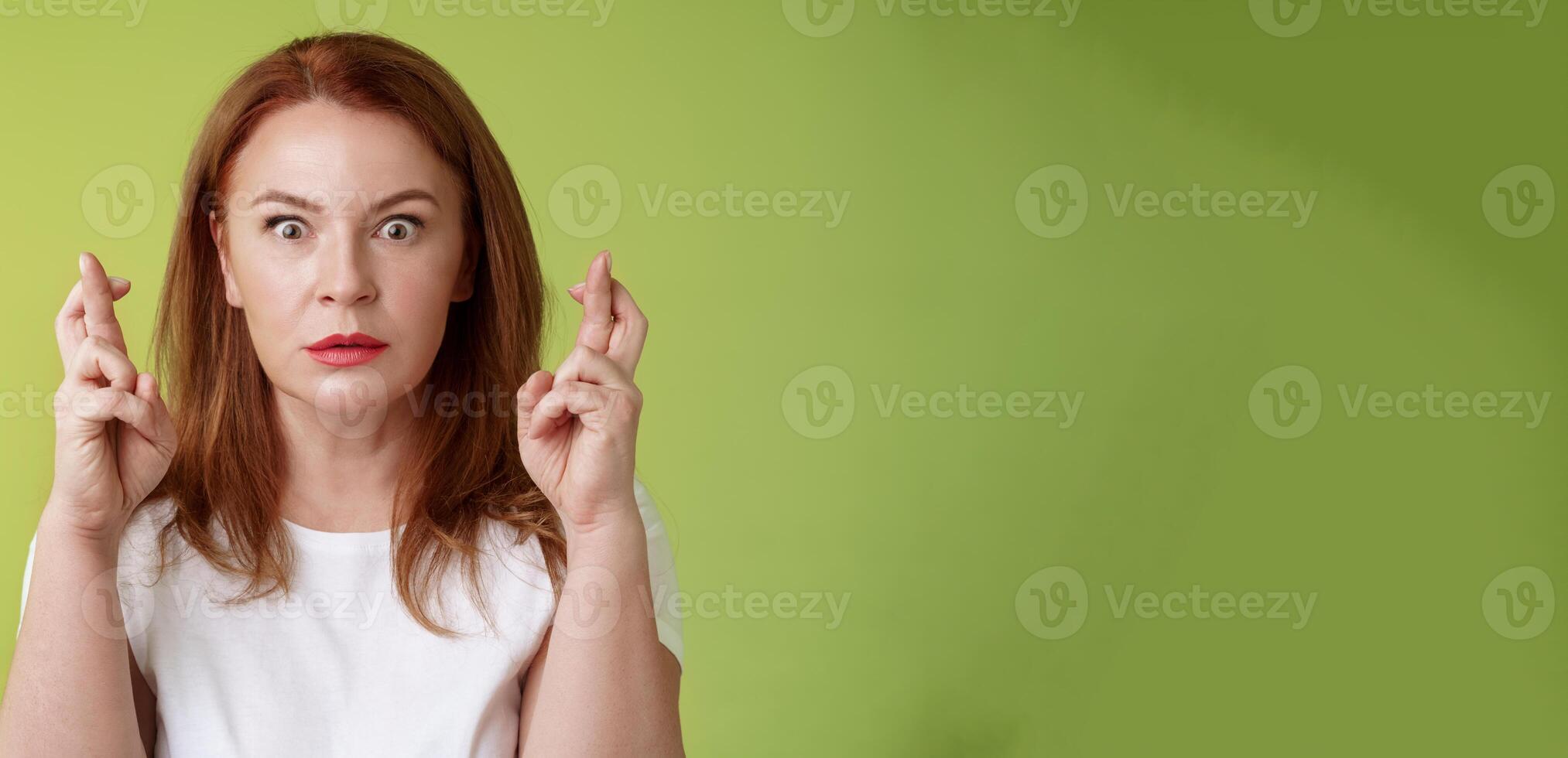 Stunned intense worried middle-aged redhead woman stare nervously awaiting important result implore dream come true receive positive reply standing stupor green background make wish good luck photo
