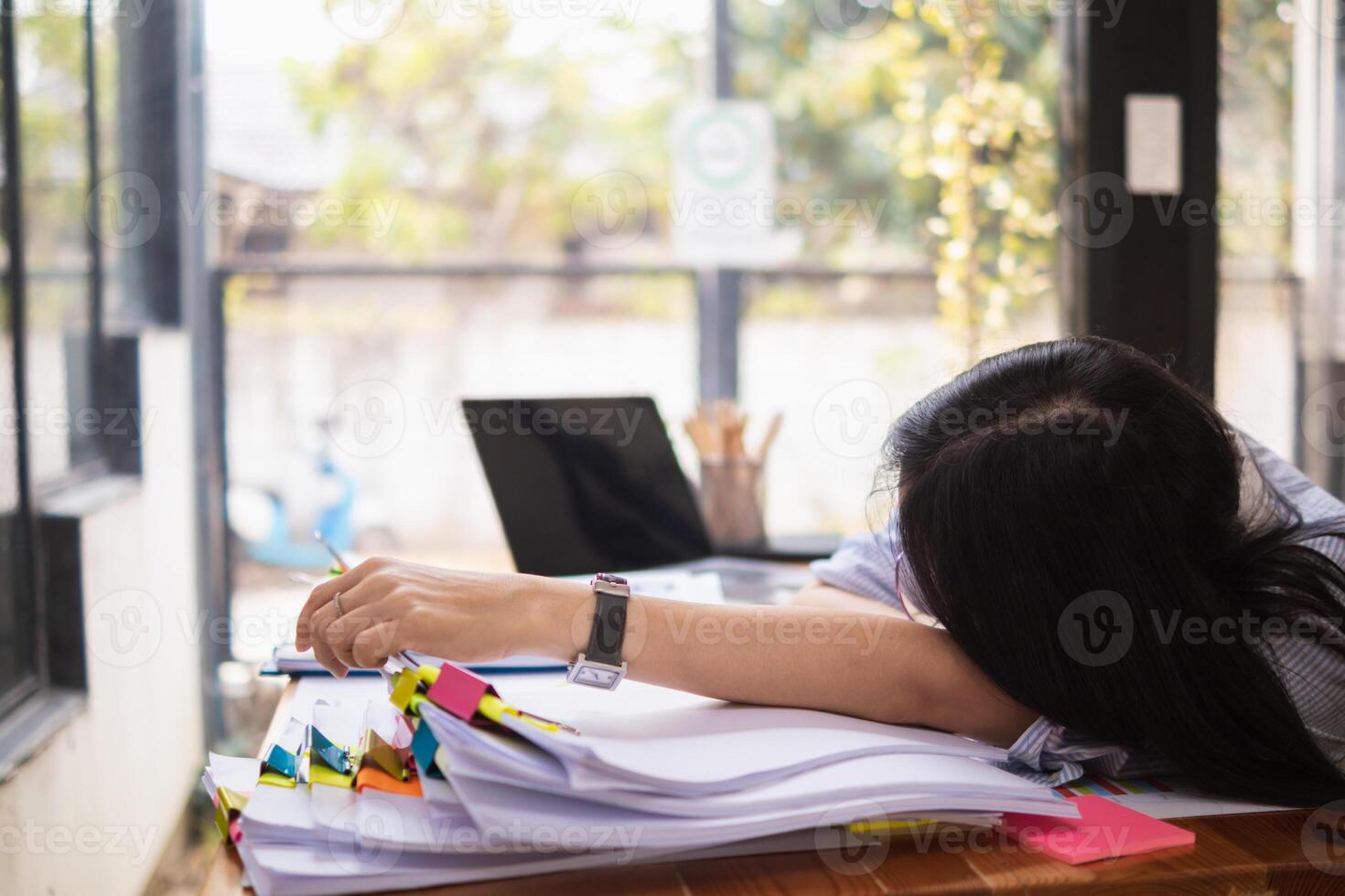 A young secretary is searching through the pile of documents on her desk to prepare for an executive meeting. The secretary looked exhausted from searching through the pile of documents on her desk. photo