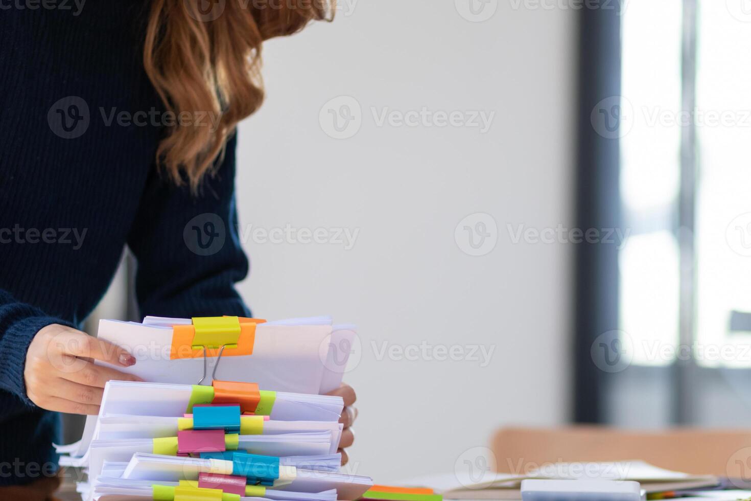 secretary is searching through pile of important documents on office table deliver them to manager for presentation in time at meeting. Concept of difficulty finding information from piles of document photo