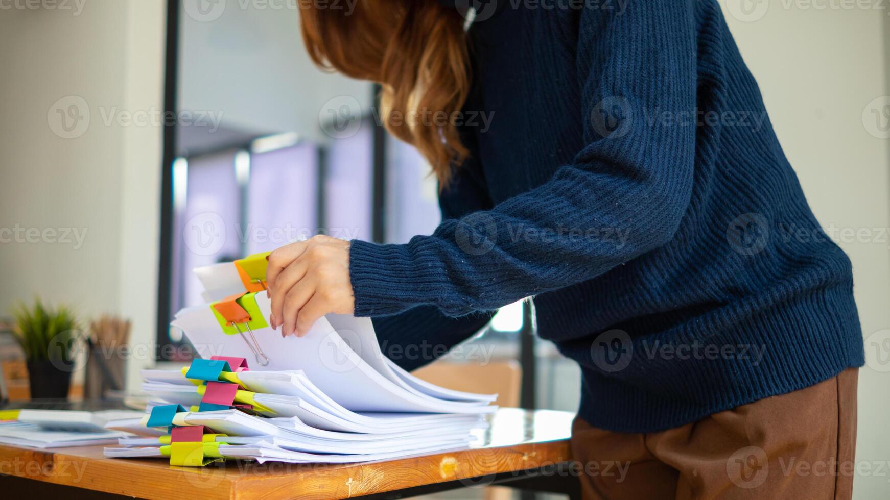 secretary is searching through pile of important documents on office table deliver them to manager for presentation in time at meeting. Concept of difficulty finding information from piles of document photo