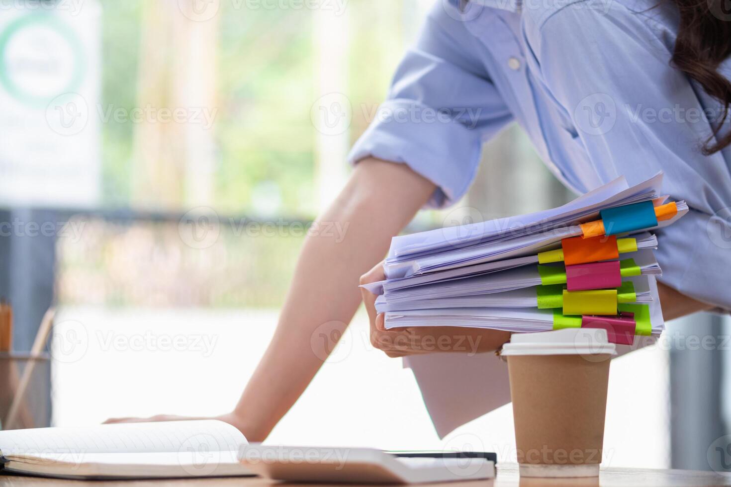 A young secretary is searching through the pile of documents on her desk to prepare for an executive meeting. The secretary looked exhausted from searching through the pile of documents on her desk. photo