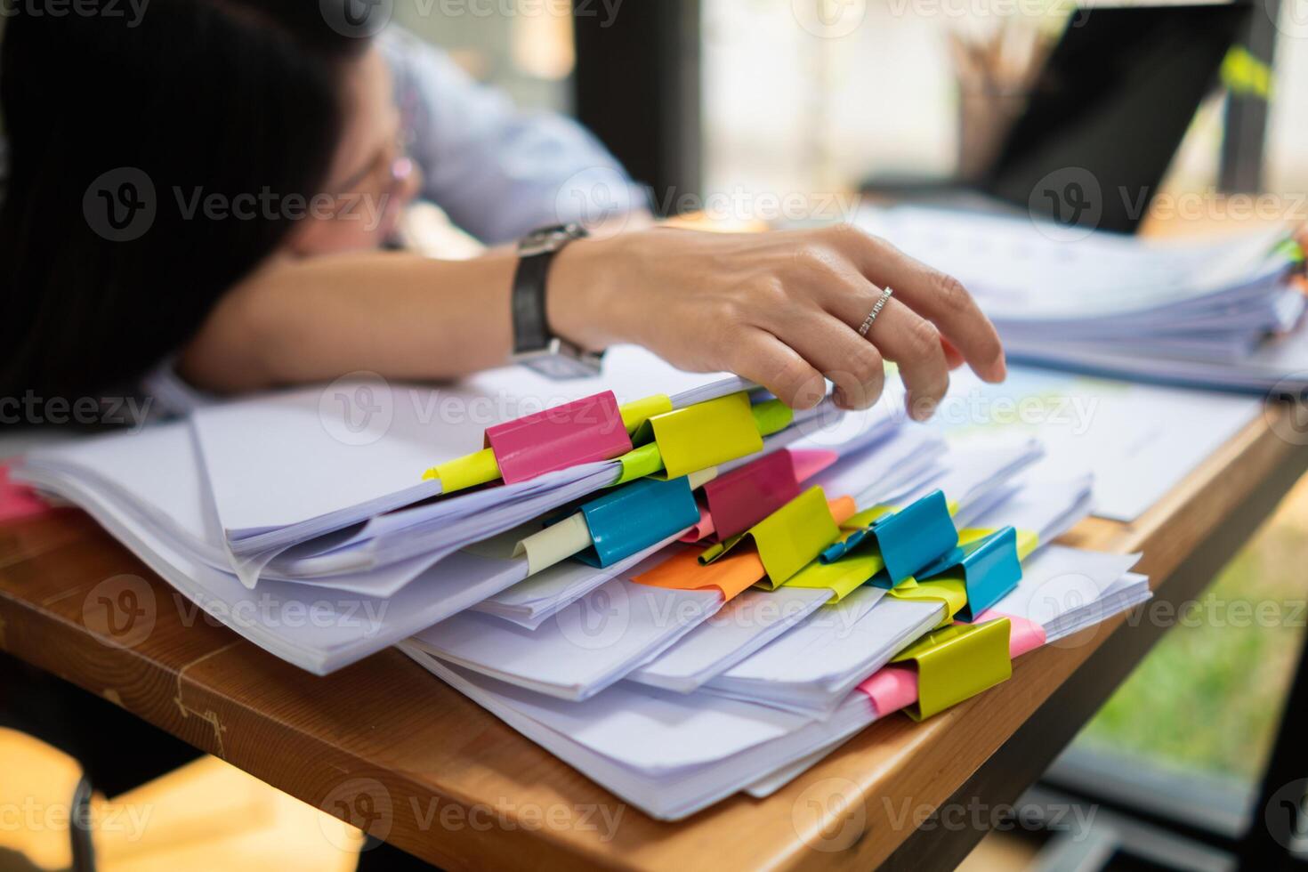 A young secretary is searching through the pile of documents on her desk to prepare for an executive meeting. The secretary looked exhausted from searching through the pile of documents on her desk. photo