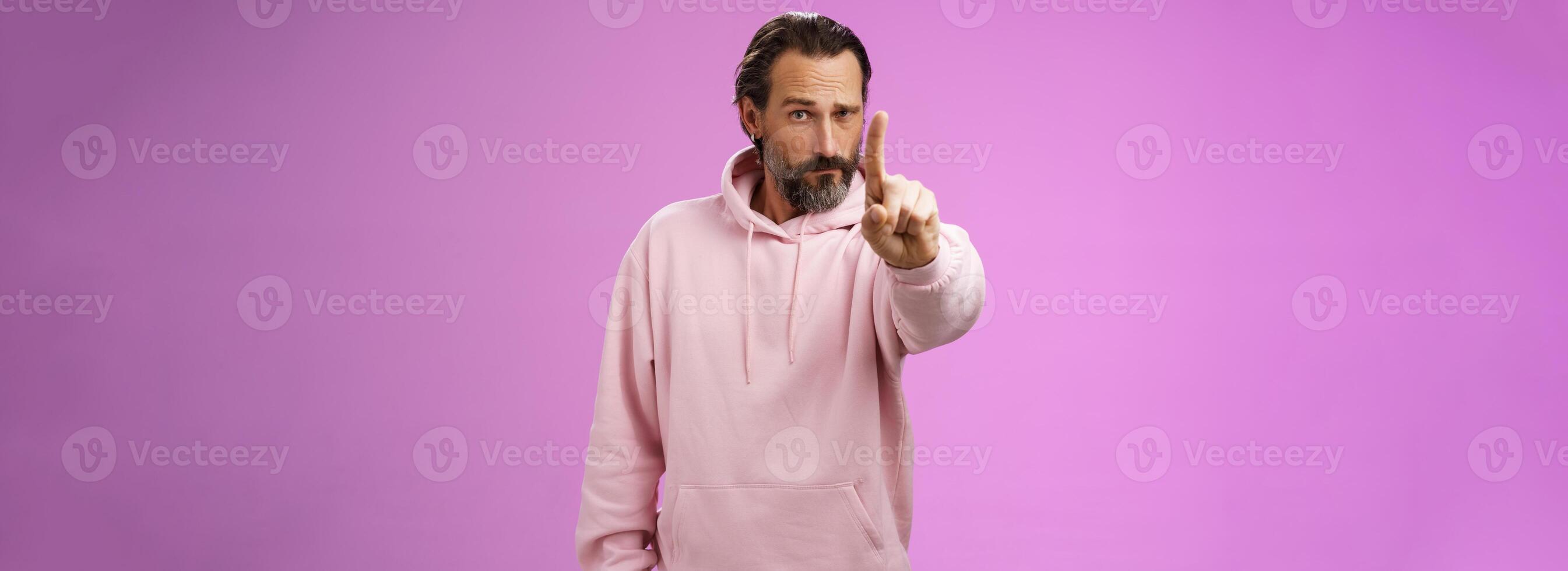 One rule listen. Serious-looking bossy focused determined adult bearded male in pink hoodie extend index finger first number scolding making statement forbid bad behaviour, purple background photo