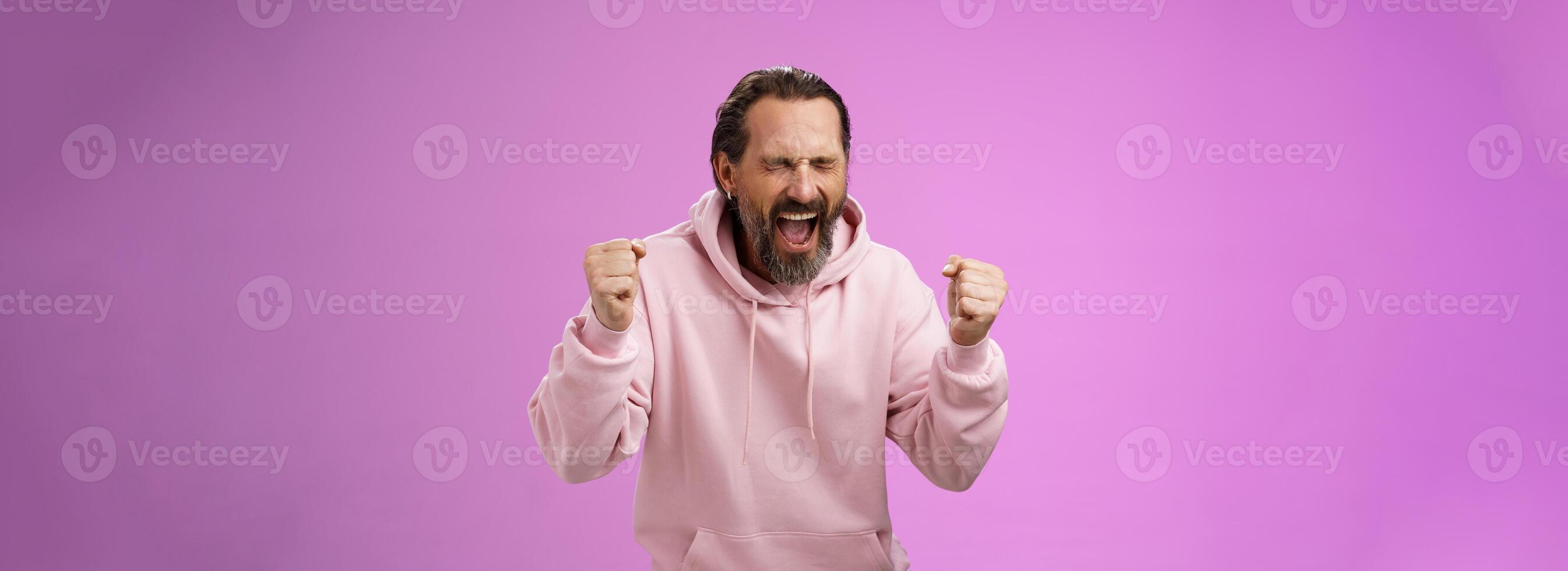 Accomplished happy joyful triumphing mature 40s bearded man grey hair yelling yes thrilled joyfully clench fists celebrating success win lottery become millionaire, standing purple background photo