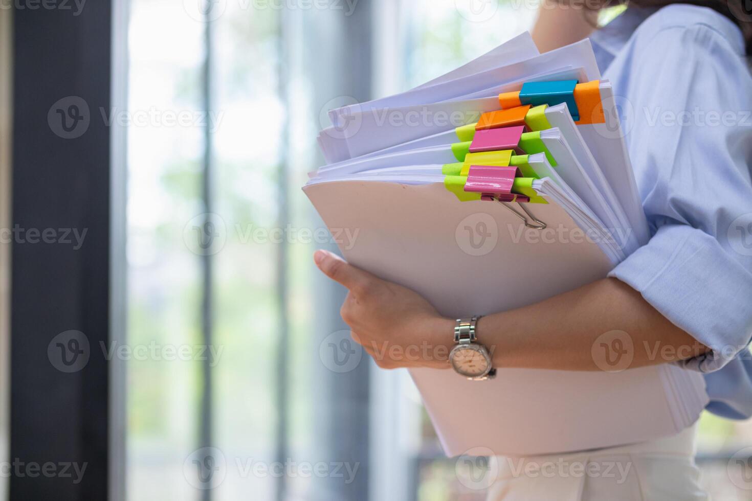 A young secretary is searching through the pile of documents on her desk to prepare for an executive meeting. The secretary looked exhausted from searching through the pile of documents on her desk. photo