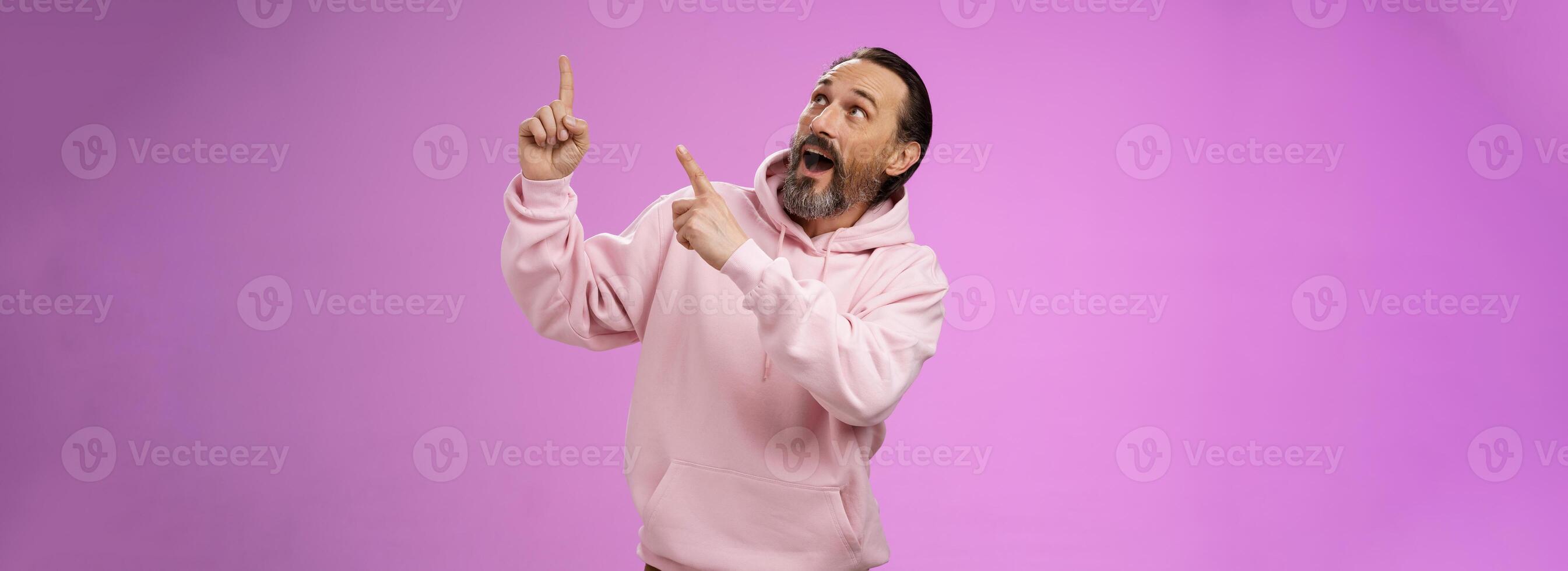 Enthusiastic energized charismatic grandfather bearded grey hair in hipster modern hoodie pointing looking impressed fascinated upper right corner discussing interesting fashion trends photo