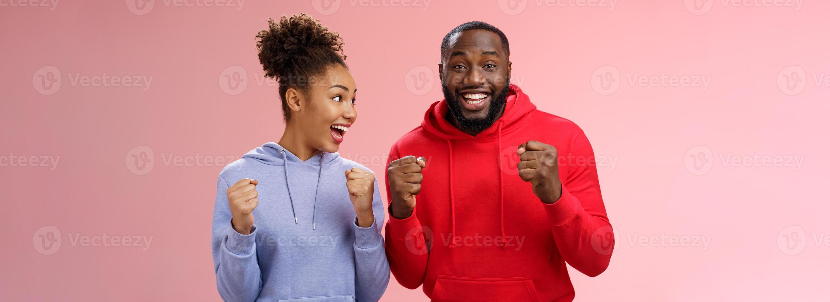 Joyful delighted celebrating african-american woman man standing together happy triumphing clenching fists cheering for favorite team watching match supporting fans celebrating goal win bet photo