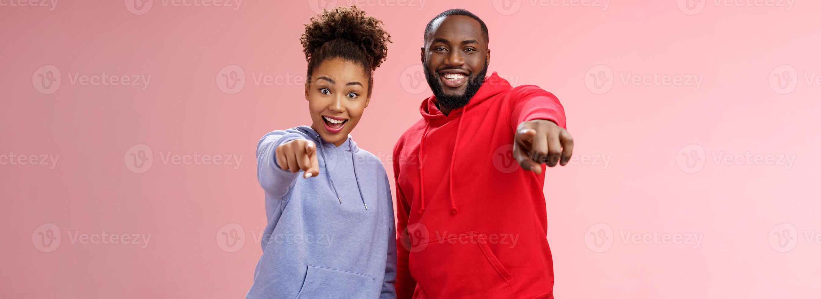 Joyful young attractive happy african-american couple vacation enjoying interesting tour standing impressed amazed pink background pointing index fingers camera awesome curious object photo