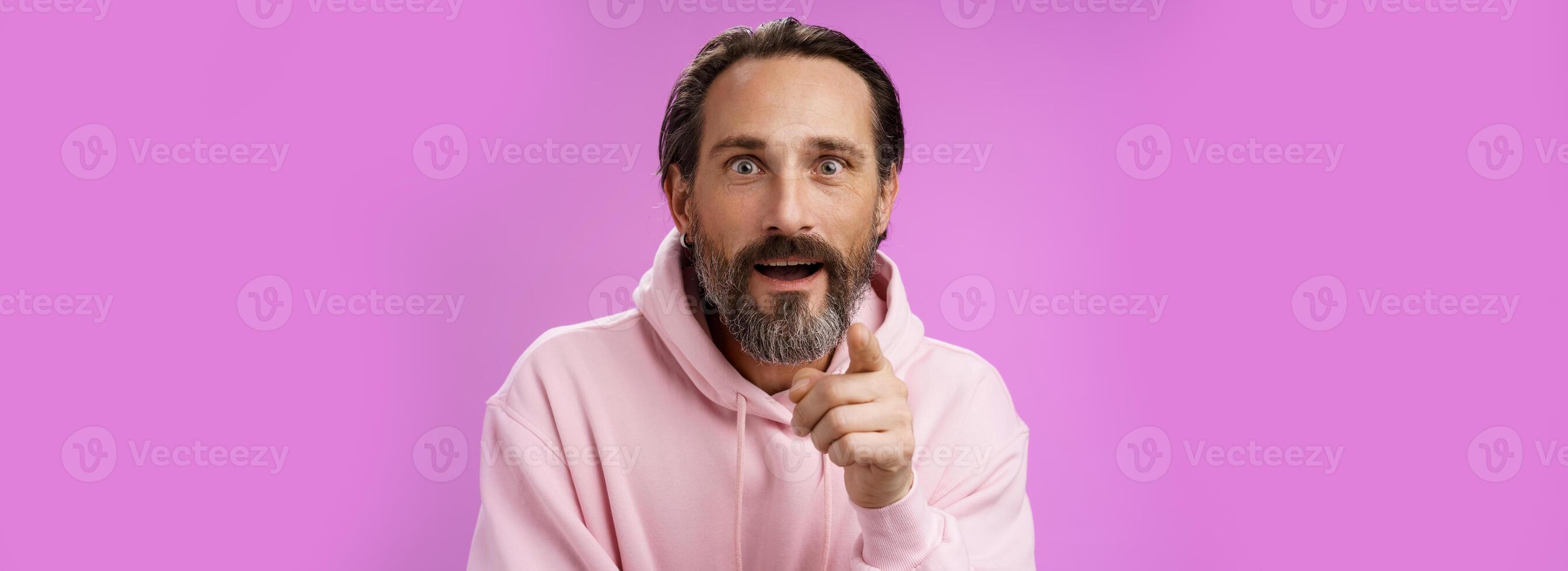 Fascinated amused european bearded mature guy widen eyes shocked open mouth recognize person pointing camera index finger surprised see familiar famous star, standing purple background photo