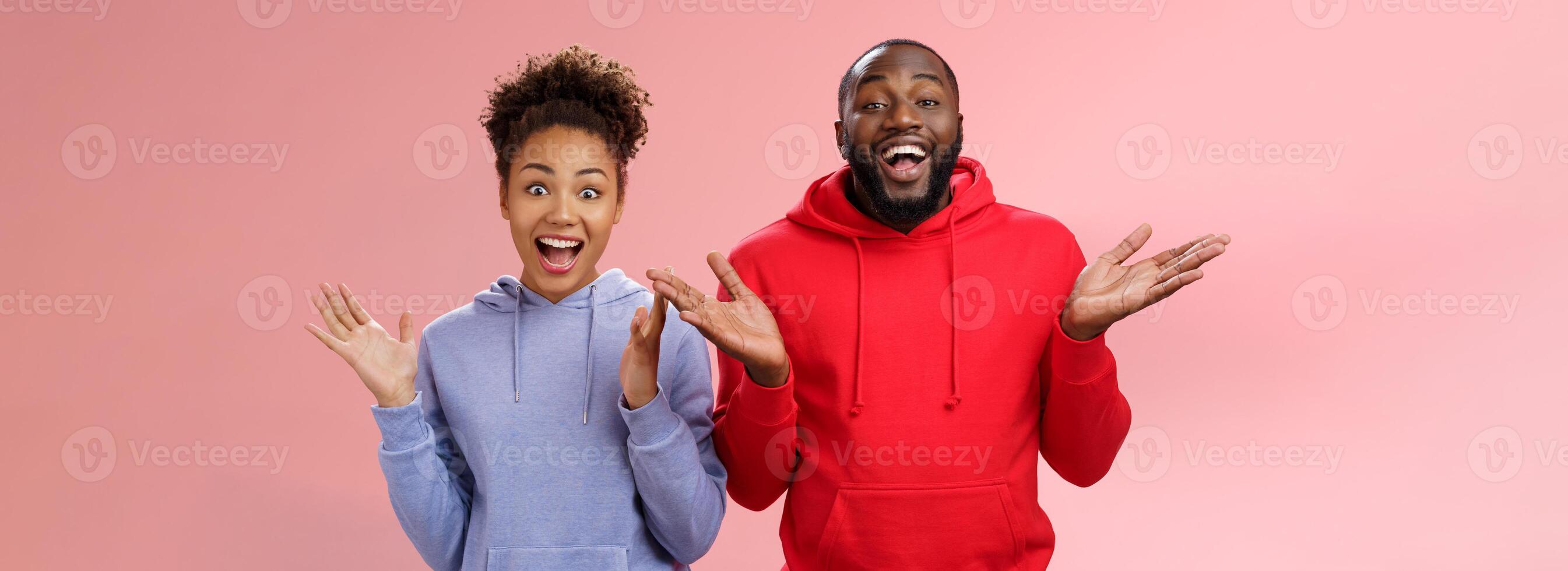 Guys receive nice surprise. Two attractive carefree surprised happy african man woman clapping hands joyfully greeting welcoming guests inviting people joing party standing friendly pink background photo