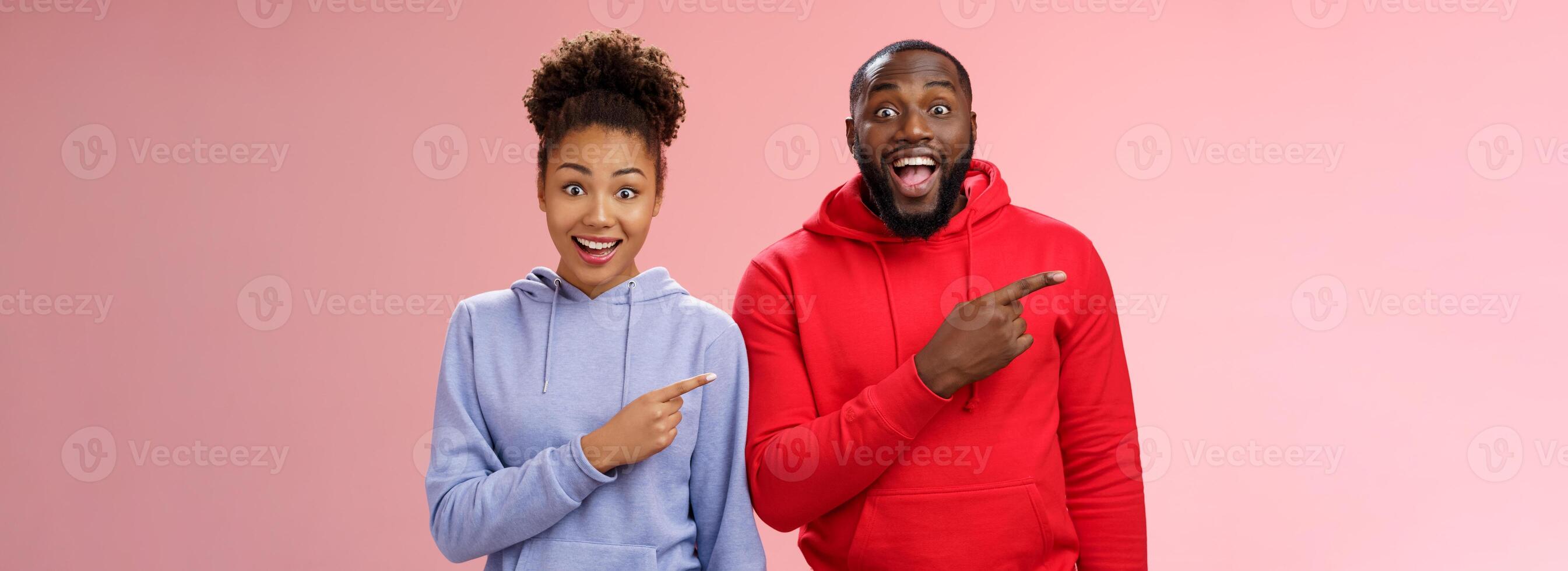 impresionado dos mejor amigos africano americano hombre mujer 25 s soltar mandíbula divertido visitar increíble interesante parque señalando izquierda índice dedos ensanchar ojos emocionado teniendo divertido juntos, en pie rosado antecedentes foto