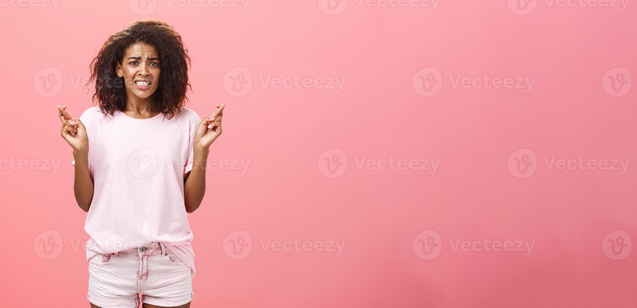 Hope she gets positive result. Portrait of worried intense hopeful good-looking young african american female coworker frowning clenching teeth and crossing fingers for good luck while making wish photo