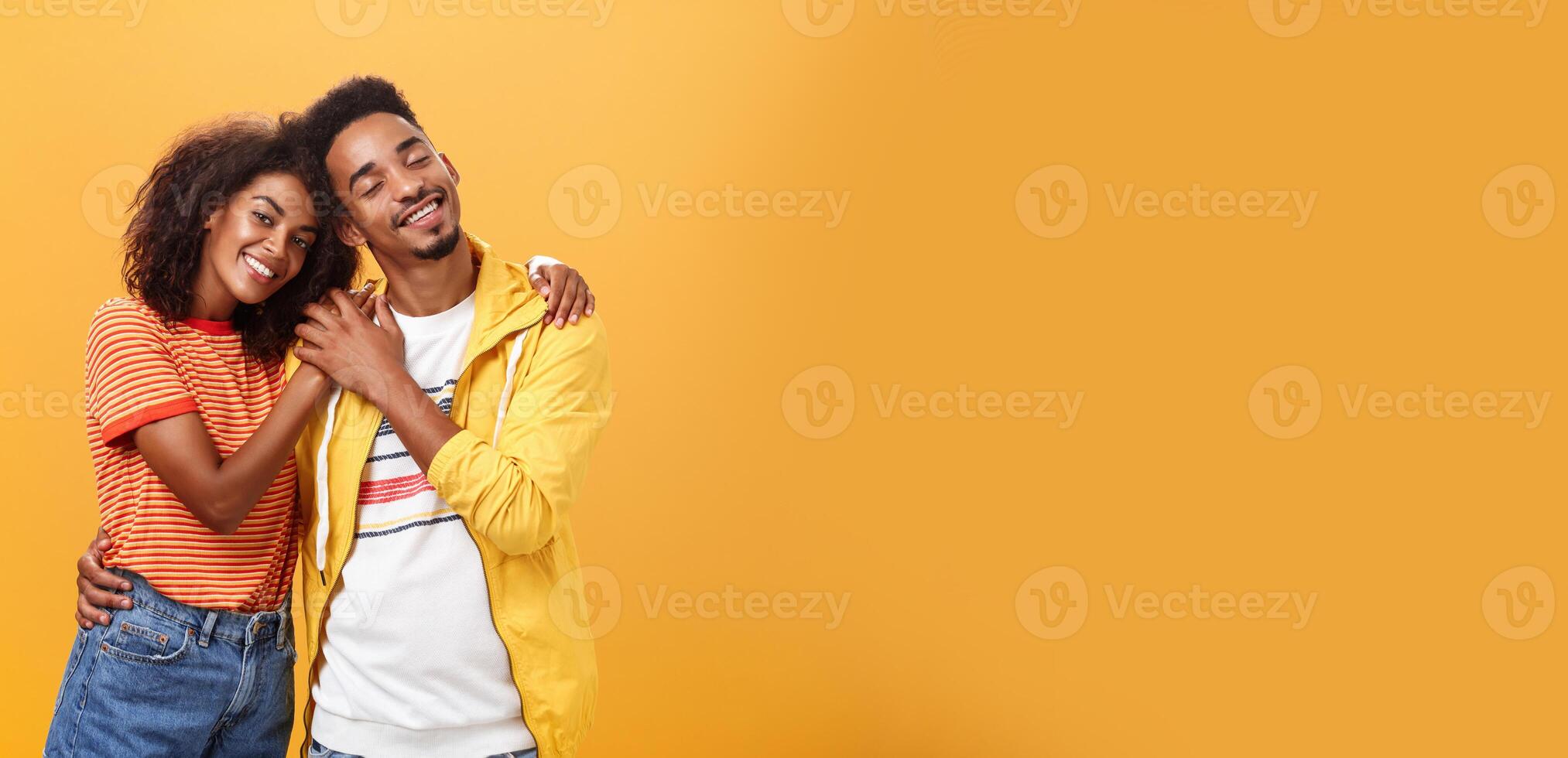 They love each other. Portrait of two charming african american man and woman in relationship hugging with heartwarming smile touching hands smiling gently posing against orange background photo