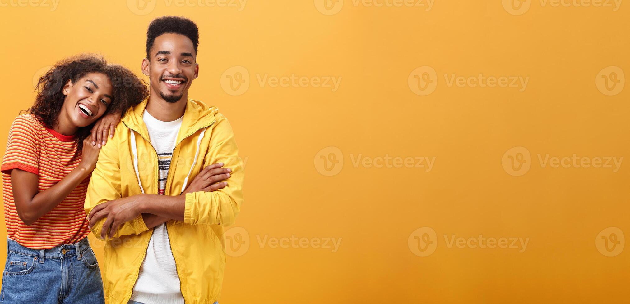 Awesome when boyfriend is best friend. Portrait of charming friendly african american woman leaning on guy touching his shoulder feeling happy they together and she can rely on posing orange wall photo
