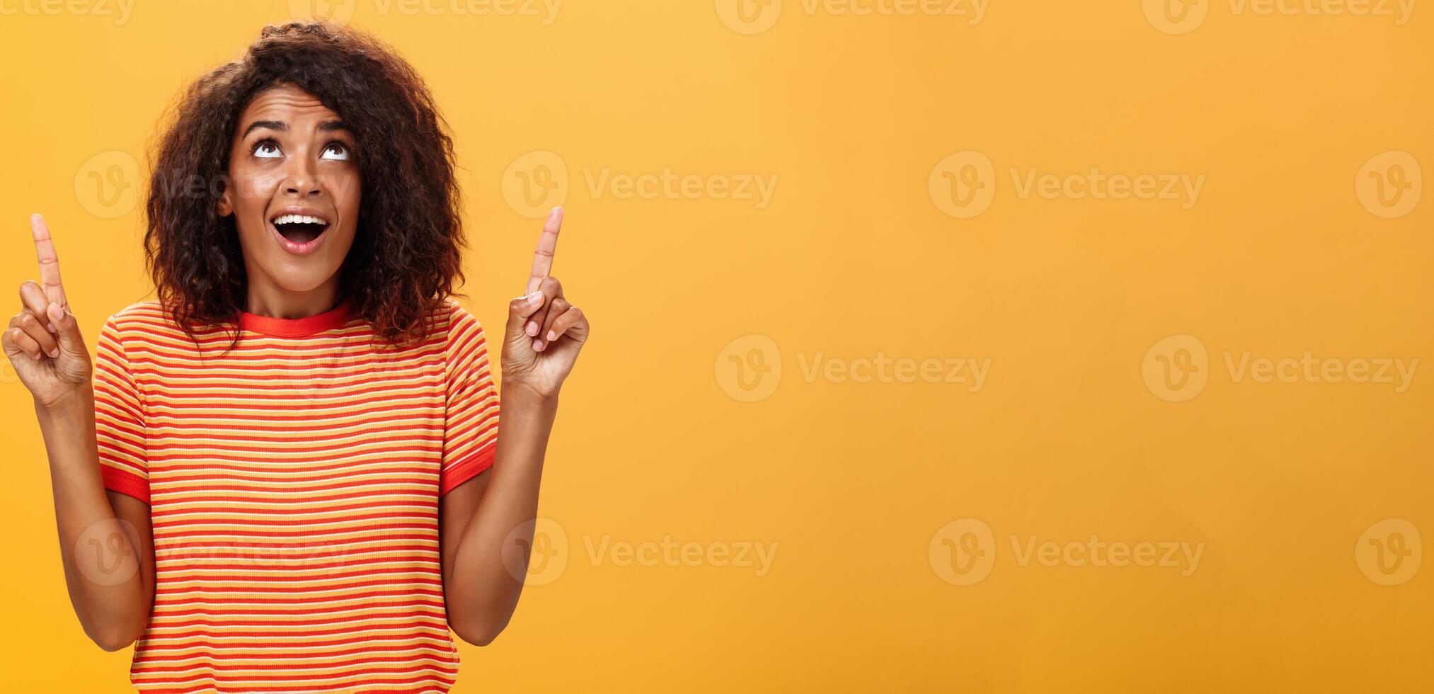 Optimistic happy african american girl saying thanks to god looking and pointing up pleased and carefree starting day in productive way being delighted with lucky chance over orange background photo