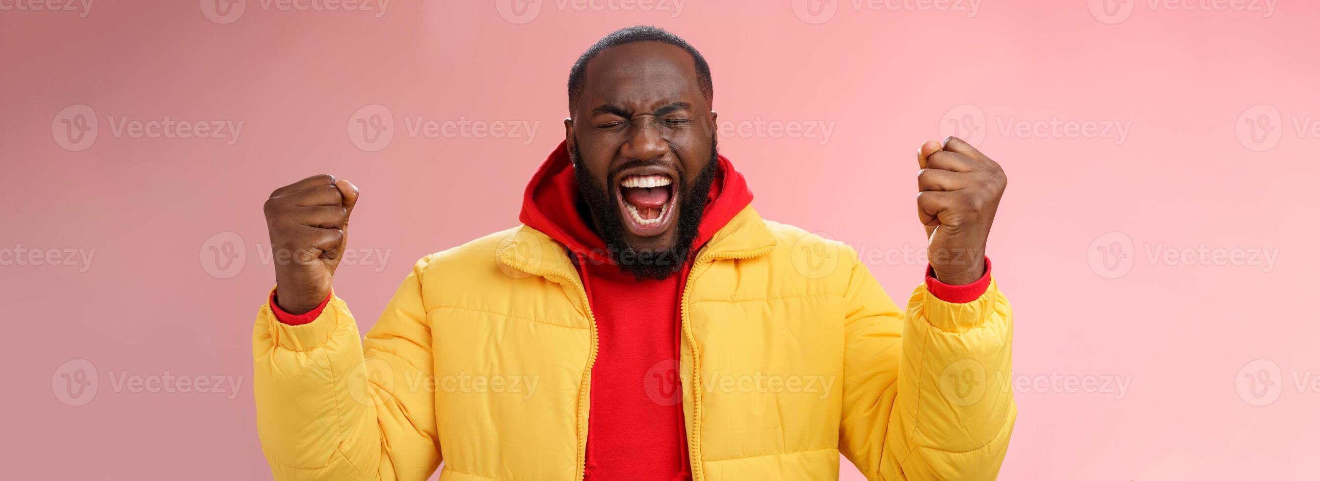 Handsome african-american man encouraging himself put will effort clenched arms yelling close eyes raise hands boost confidence, standing pink background express rage release emotions photo