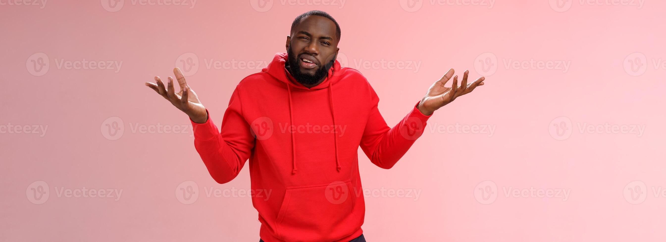 Bothered pissed african american bearded boyfriend in red hoodie arguing standing questioned bothered stupid accusations shrugging raise hands dismay cringing perplexed, pink background photo