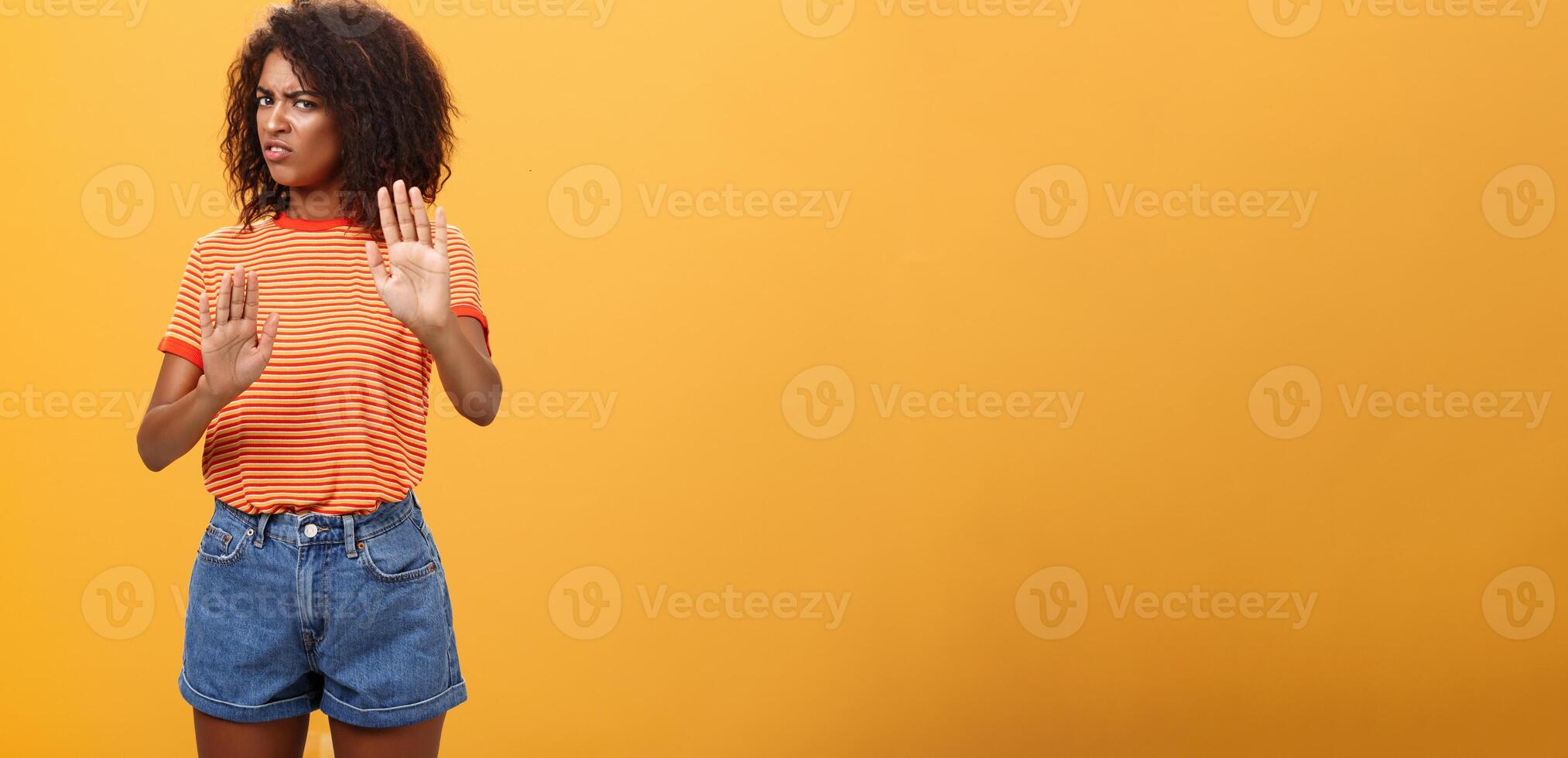 No I refuse. Intense suspicious and displeased smart african-american female rejecting bad offer pulling raised palms turning away with aversion and dissatisfied look against orange background photo