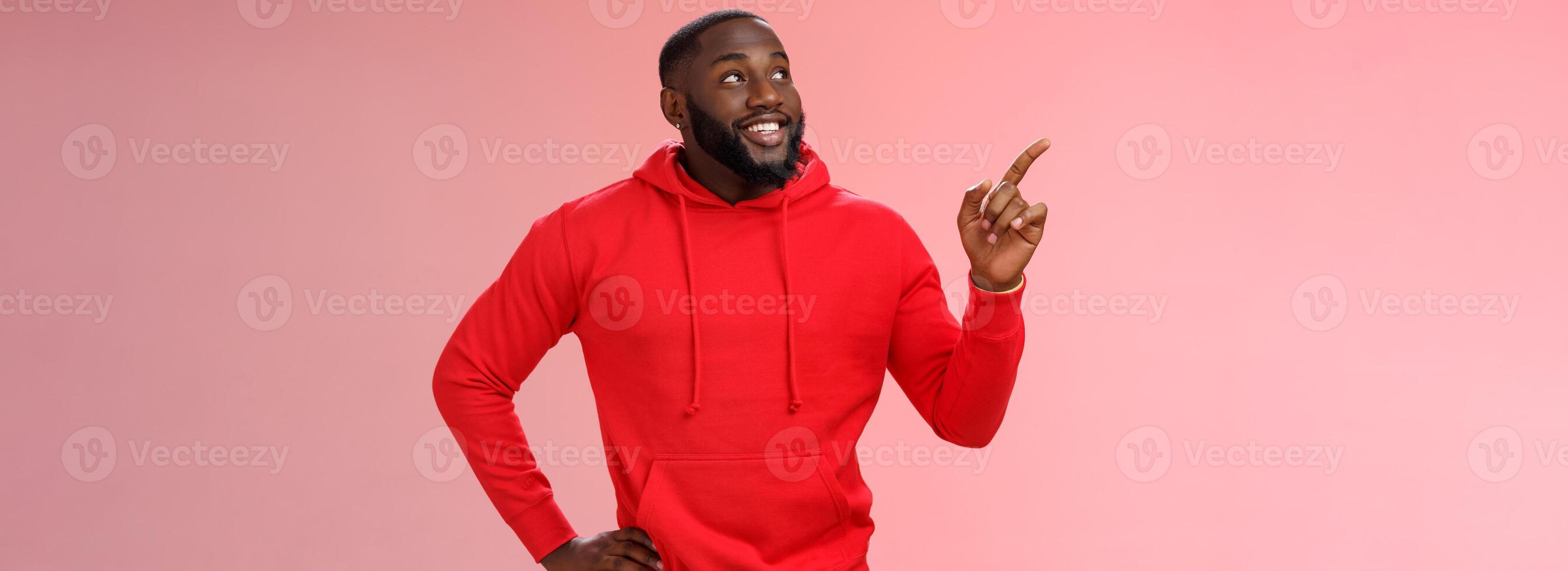 Happy charismatic delighted african-american bearded guy smiling white teeth look pointing intrigued upper left corner curious what interesting product standing impressed pink background photo