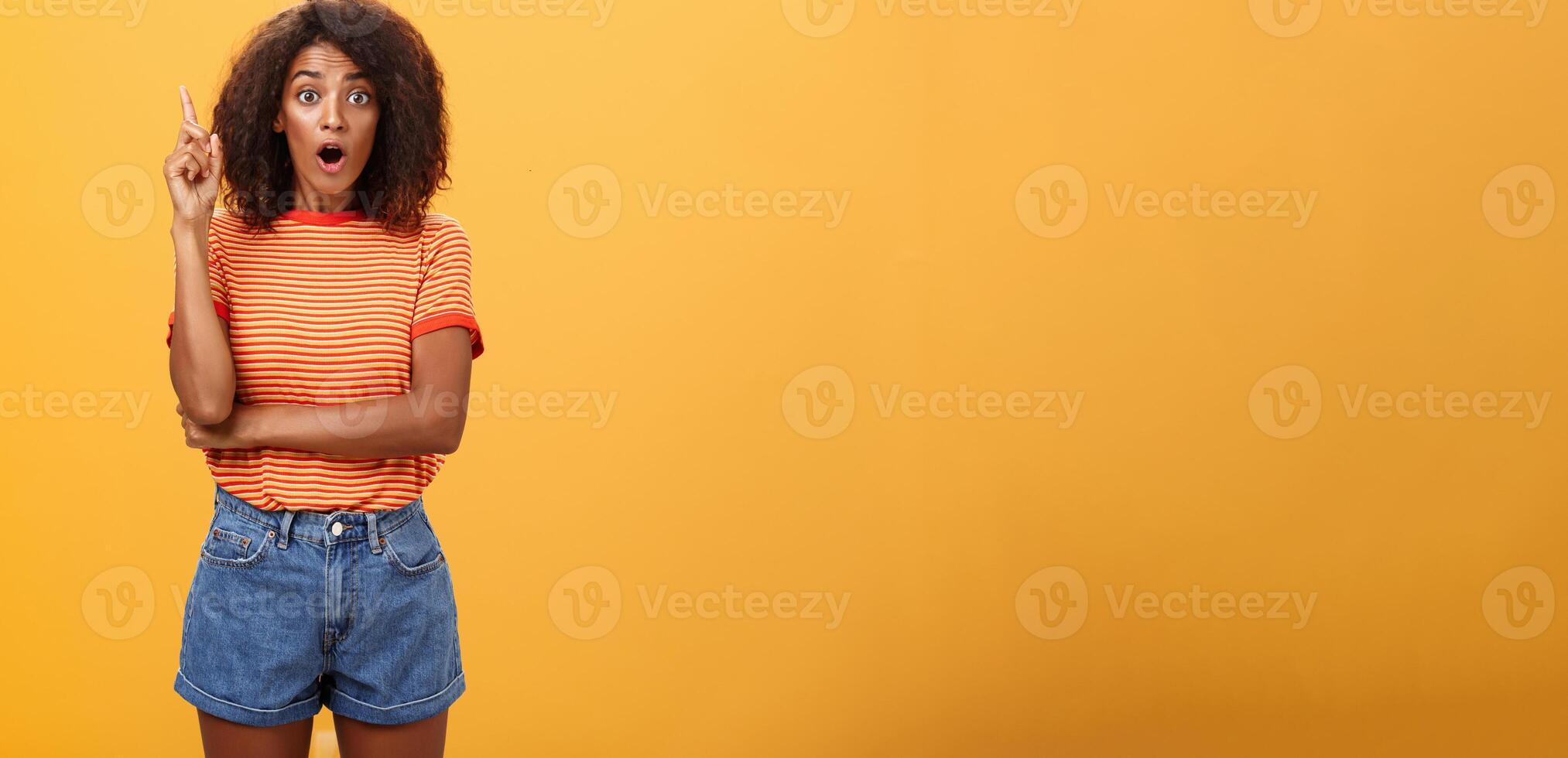 Girl finally understood riddle adding suggestion outloud. Excited thrilled good-looking dark-skinned woman staring amazed raising index finger in eureka gesture having idea over orange wall photo