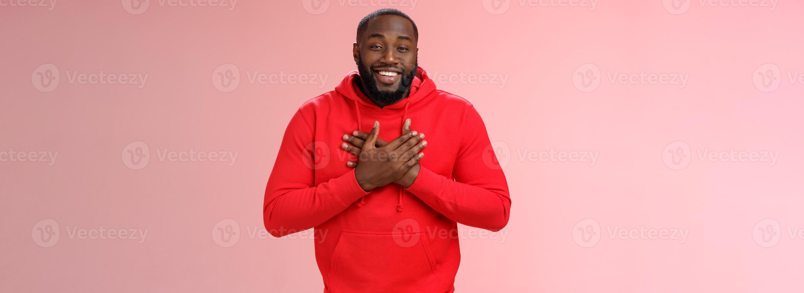 Pleased touched african american smiling young bearded man hold hands heart grinning thanking heartwarming lovely congratulations, receive good feedback standing happy thanking everyone photo