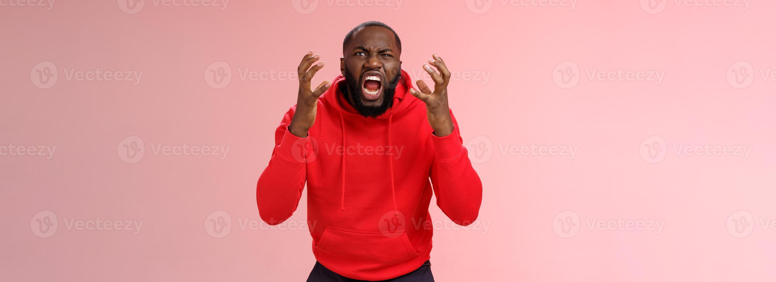 chico odia subterraneo. irritado hambriento enojado barbado afroamericano hombre Gritando apretar puños ceñudo haciendo muecas gritos perdiendo templar furiosamente curioso cámara Vamos loco loco, en pie rosado antecedentes foto