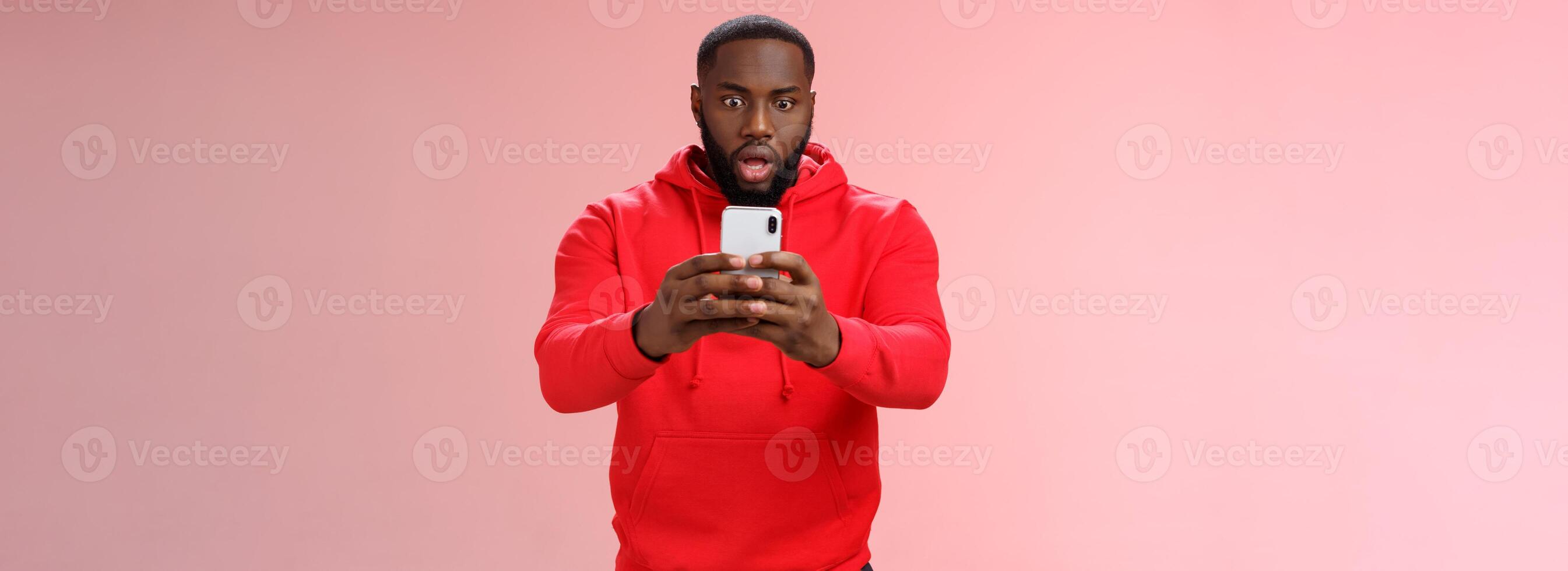 Wow hold on let take picture. Portrait impressed surprised shocked man capturing shocking situation holding smartphone look display recording sensational video, standing pink background photo