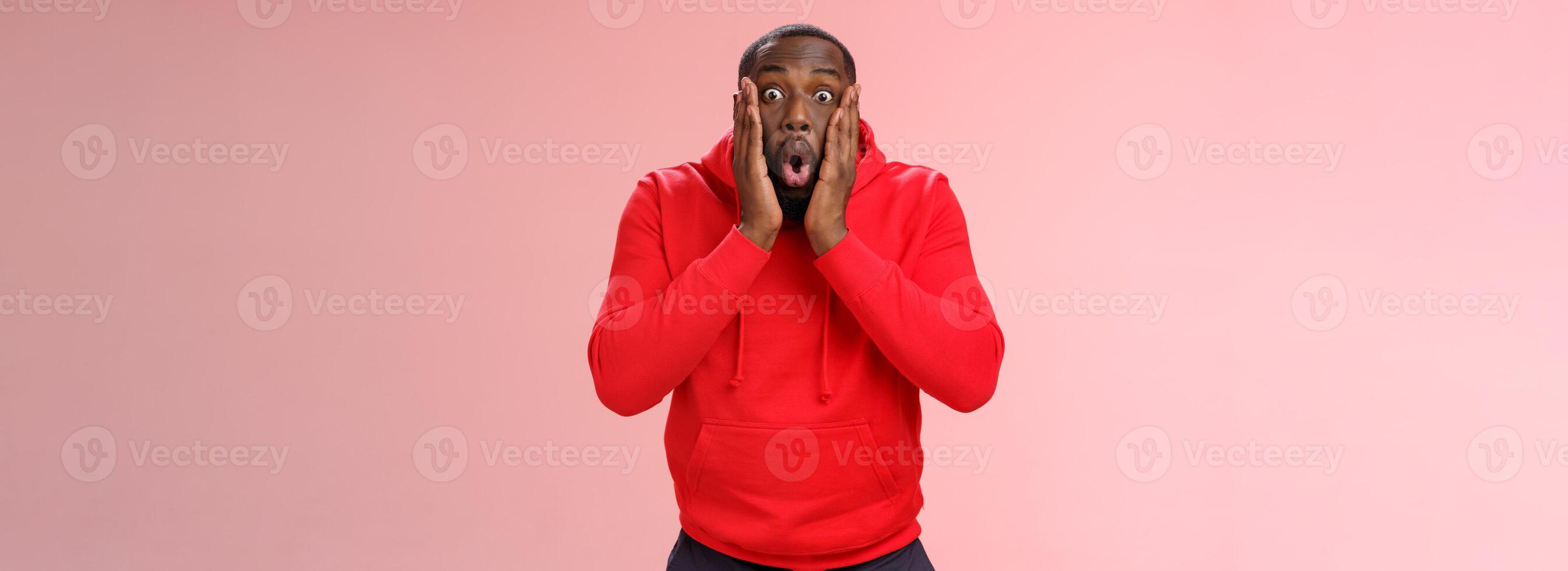 Wow incredible. Portrait impressed surprised african-american bearded guy in red hoodie folding lips bending widen eyes shocked see incredible offer standing amused excited, pink background photo