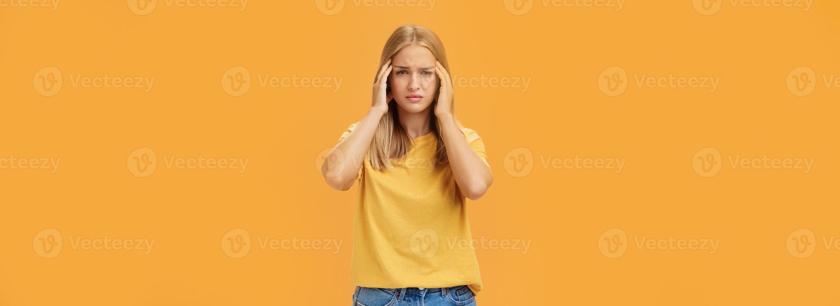 Portrait of drained sad young woman with tanned skin and fair hair feeling discomfort in head touching temples squinting and looking sick suffering headache or migraine trying concentrate on work photo