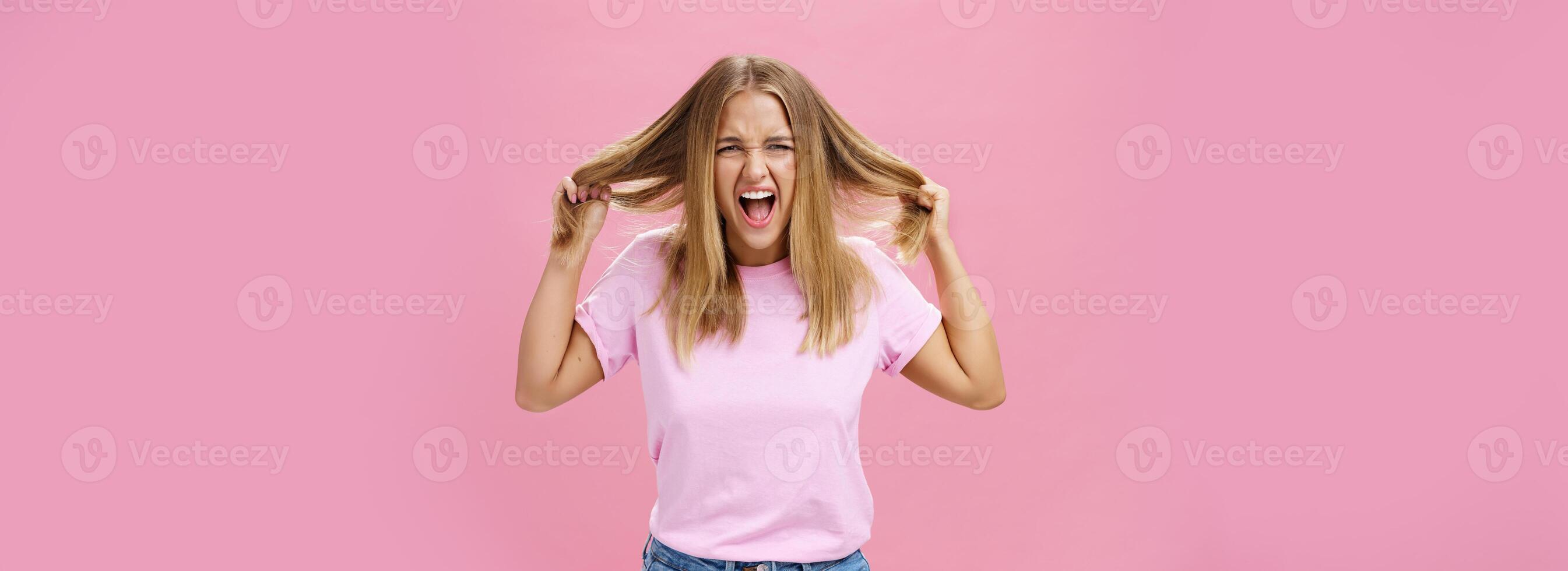 Portrait of pissed outraged and irritated woman losing temper feeling pressured screaming from distress pulling hair out of head standing annoyed over pink background fed up doing haircut every day photo