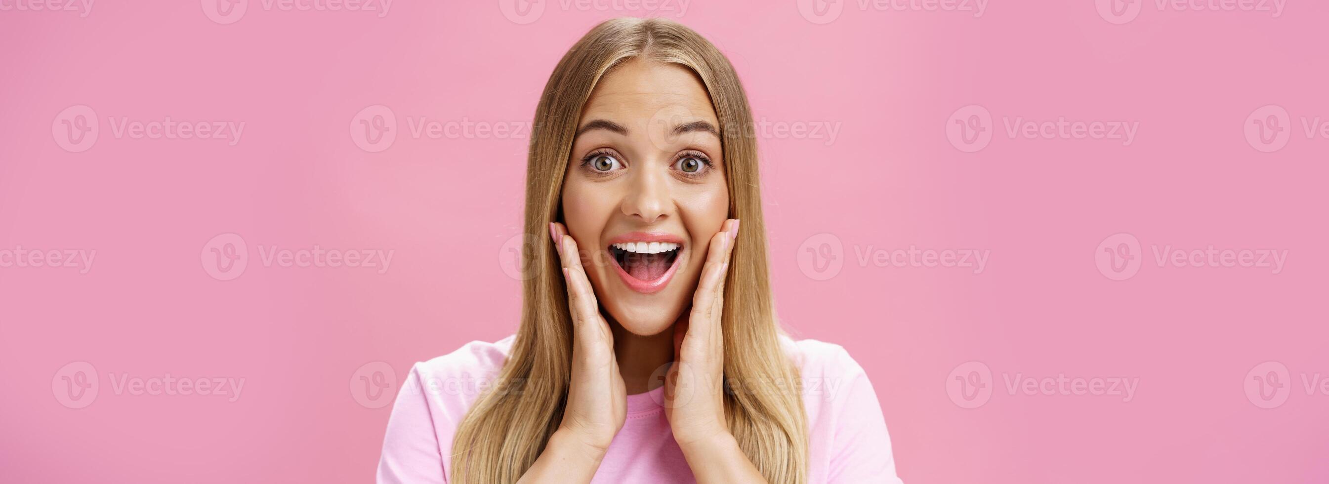 Woman surprised to see own face without imperfactions treating acne feeling beautiful and happy touching cheeks, smiling amazed, joyful looking with admiration and excitement at camera over pink wall photo