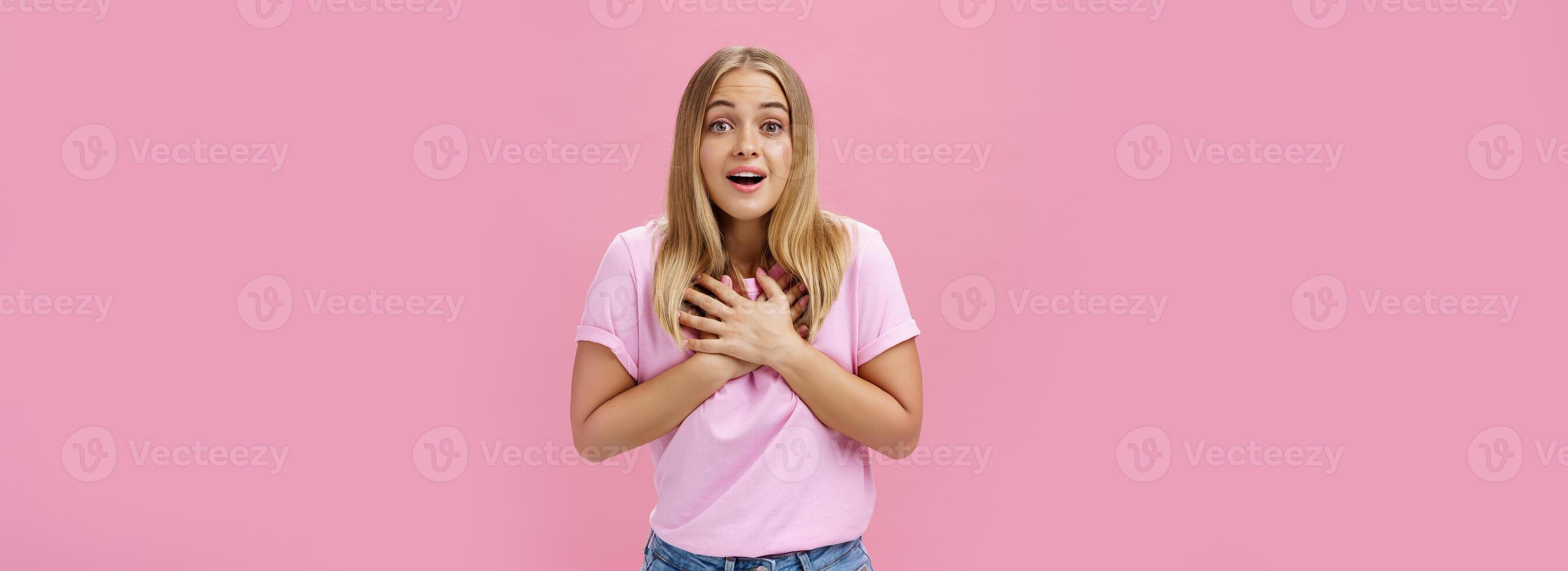 Indoor shot of touched surprised good-looking nice girl in t-shirt and jeans holding palms on heart gasping from amusement and amazement reacting to awesome pleasant news grateful and happy photo